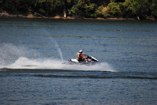A close-up of a jet ski speeding past a rocky shoreline with spray flying.