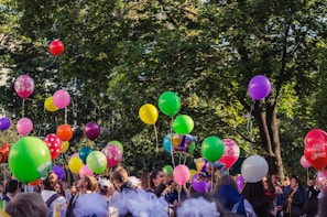 people gathering under green trees with balloons