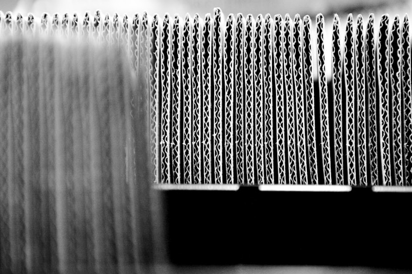 A close-up view of the edges of several stacked sheets of corrugated cardboard arranged in a row, highlighting the wavy structure of the material.