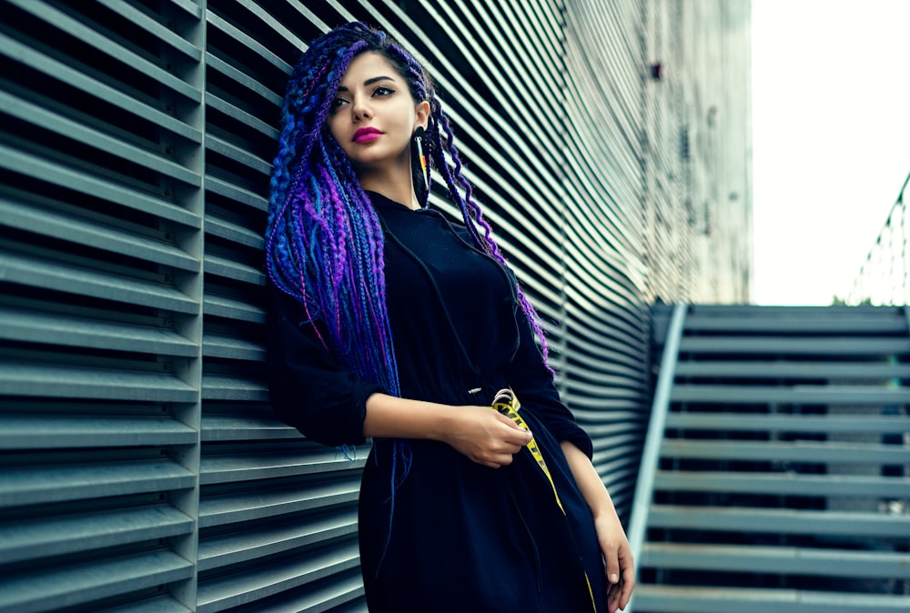 woman in black dress standing beside gray wall