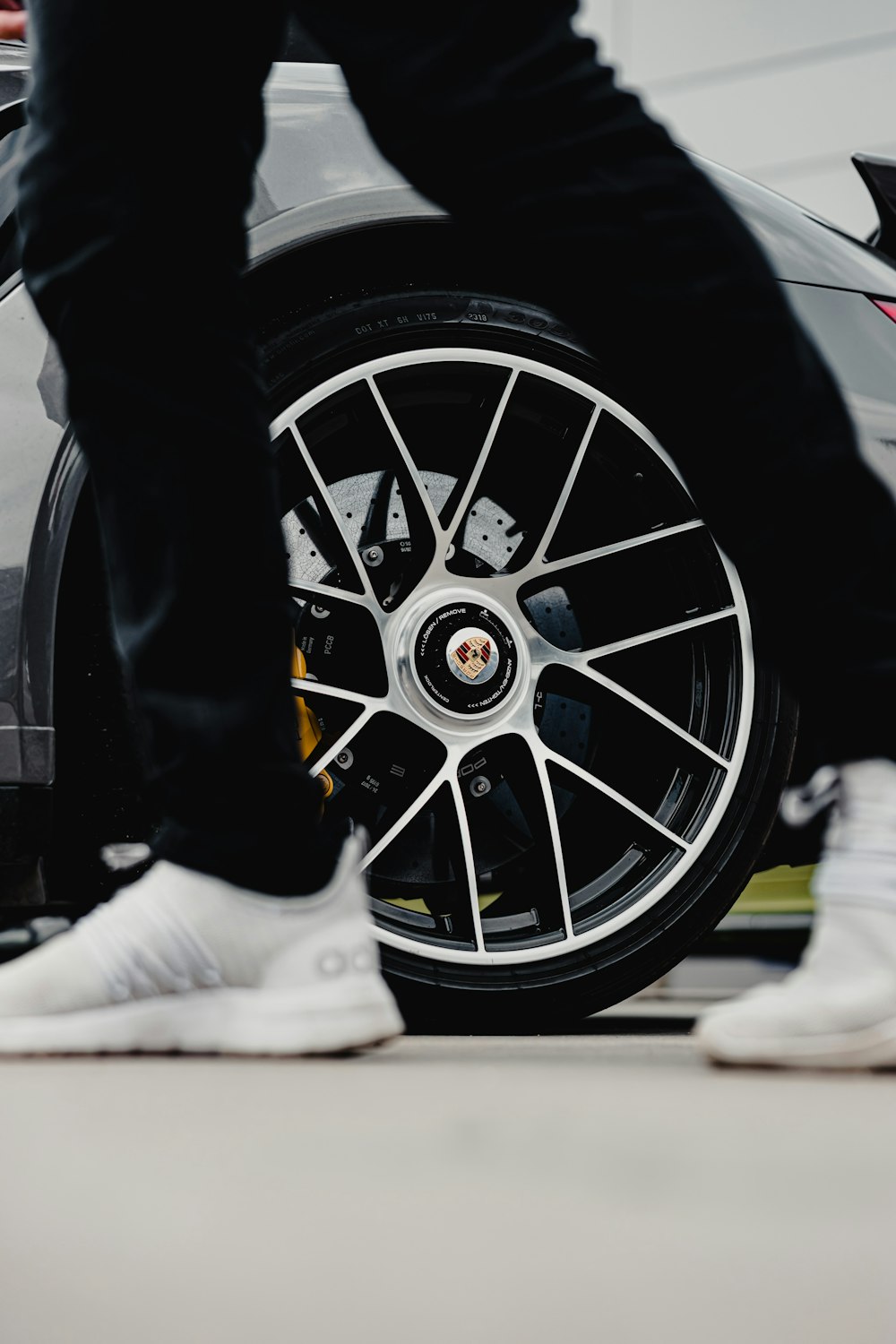 person in black pants and white shoes standing beside black and silver car wheel