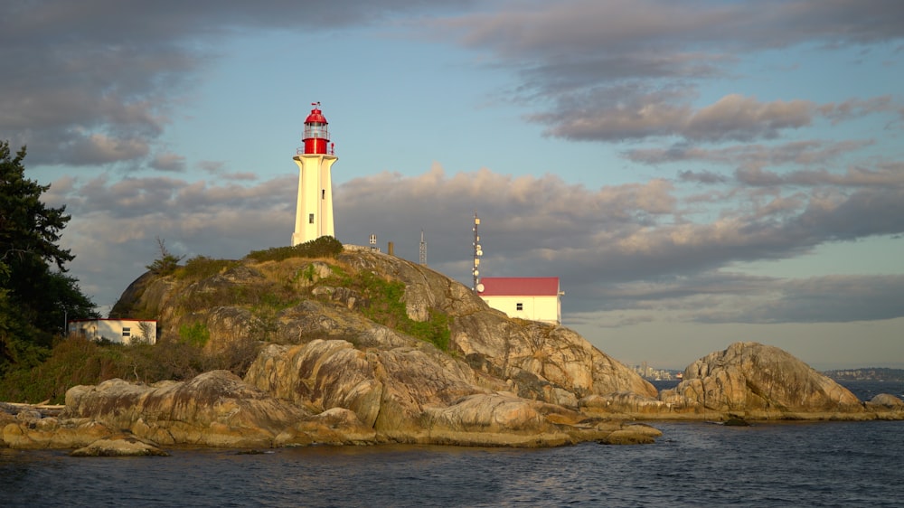 white and red lighthouse on brown rock formation near body of water during daytime