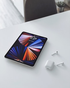 A tablet displaying a vibrant screen, placed next to a pair of headphones and a stylus pen.