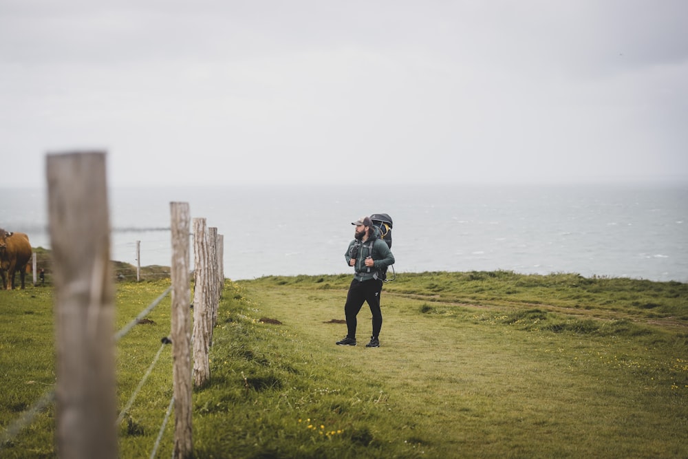 person in black jacket and black pants standing on green grass field under white sky during