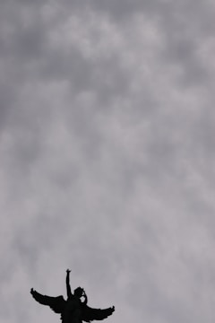 A guardian angel with glowing wings watching over a city skyline at dusk.