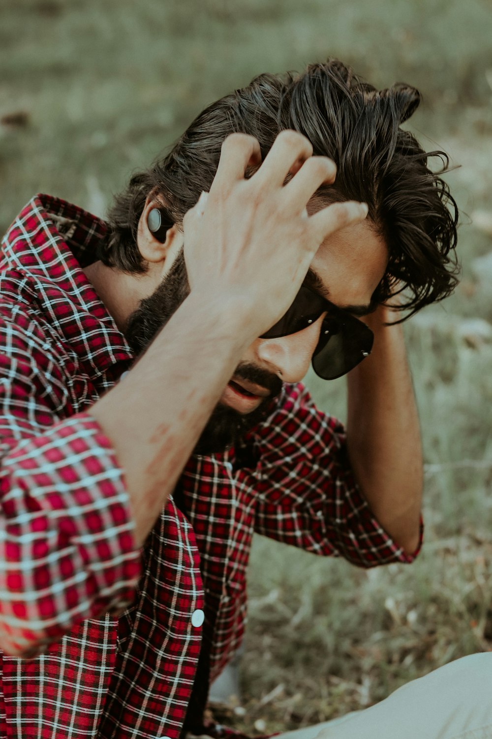 man in red and black plaid shirt covering face with his hands