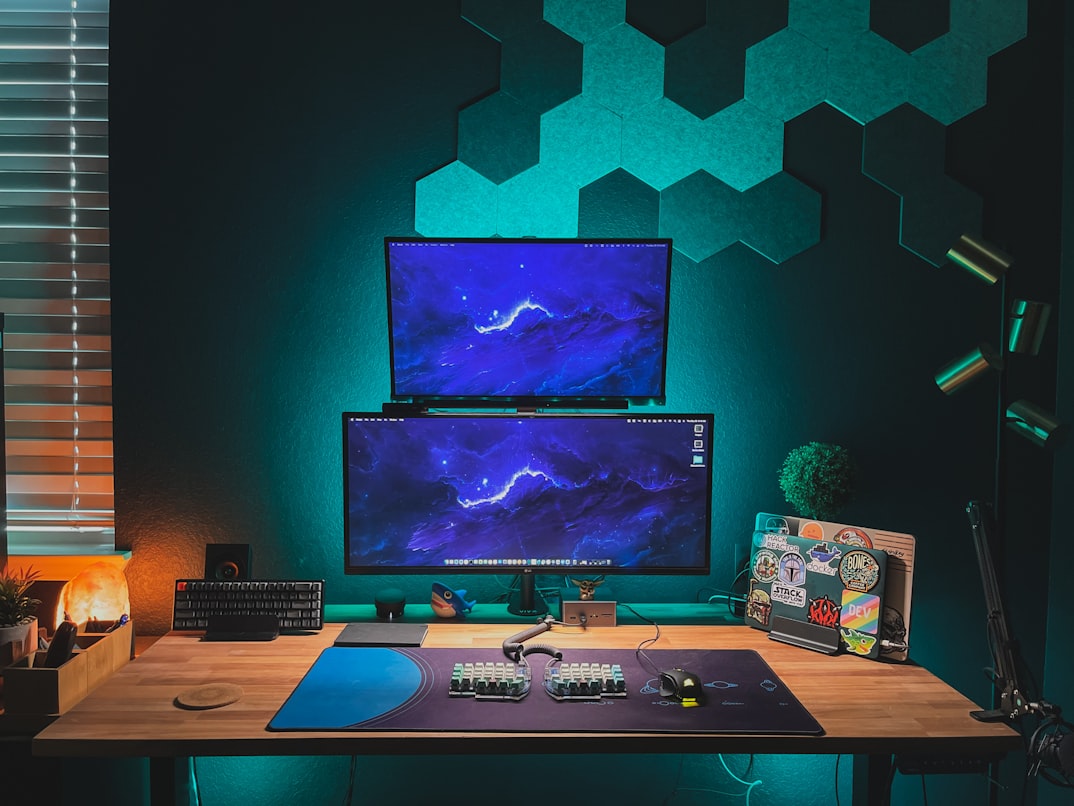 workspace with two screens displaying a blue lightning among other work stuff on a wood table, with an overall green light