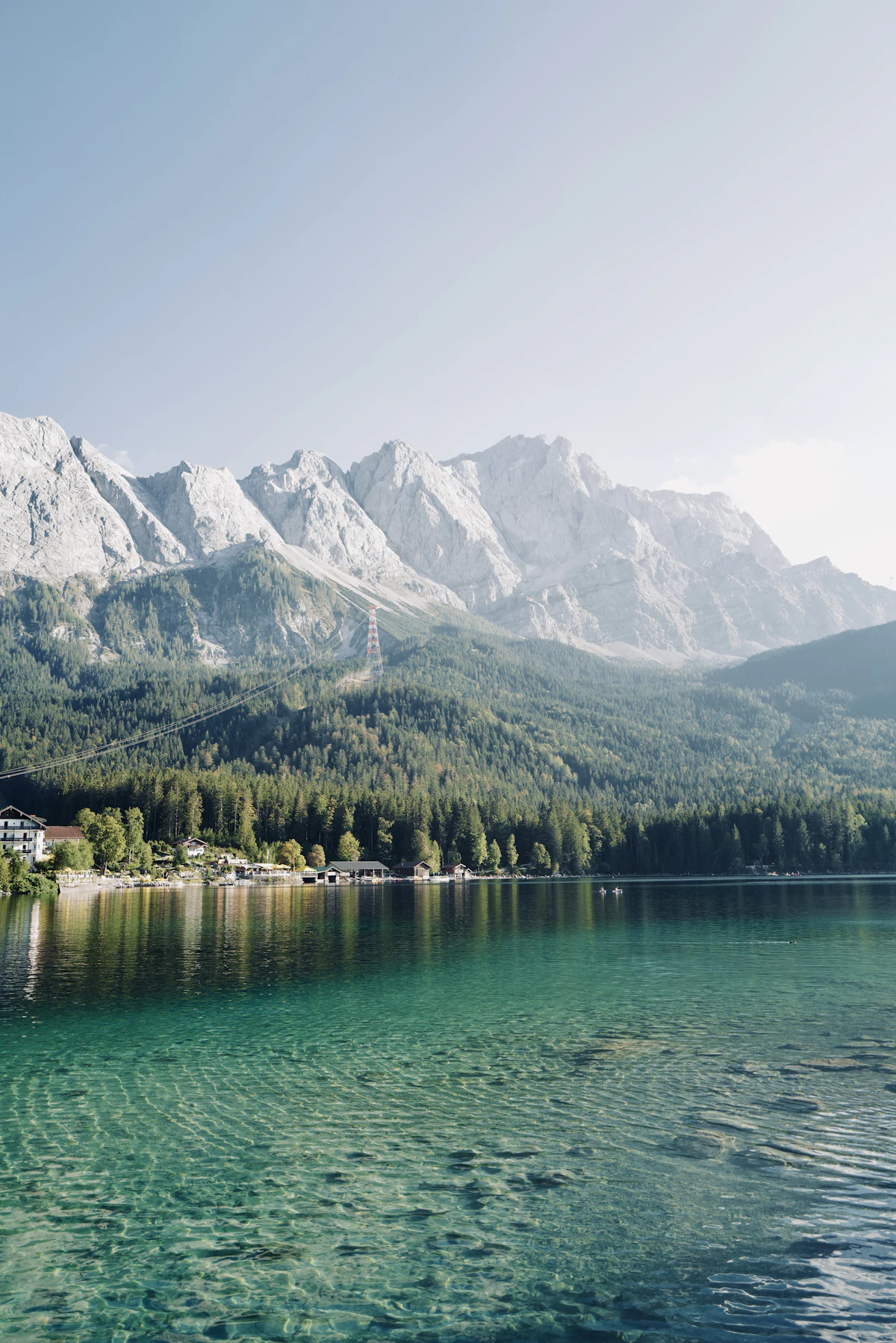 The clear green water of the Eibsee under a wall of grey rock peaks, with forest along the shore
