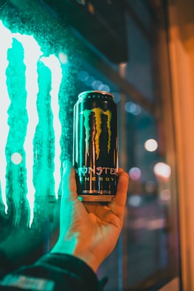 Person holding an energy drink can with a cityscape background