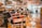 Interior of a barber shop featuring multiple vintage barber chairs lined up along a wooden floor. The walls are adorned with various signs, photos, and memorabilia, and shelves are stocked with grooming products. The space has a nostalgic and classic atmosphere.