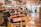 Interior of a barber shop featuring multiple vintage barber chairs lined up along a wooden floor. The walls are adorned with various signs, photos, and memorabilia, and shelves are stocked with grooming products. The space has a nostalgic and classic atmosphere.