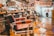 Interior of a barber shop featuring multiple vintage barber chairs lined up along a wooden floor. The walls are adorned with various signs, photos, and memorabilia, and shelves are stocked with grooming products. The space has a nostalgic and classic atmosphere.
