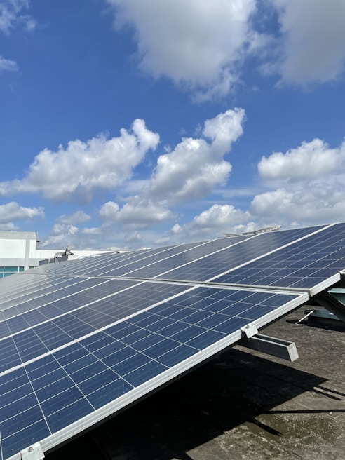 Solar panels are installed on a rooftop under a partly cloudy sky, capturing sunlight efficiently. The panels are aligned in neat rows, suggesting a modern approach to renewable energy.
