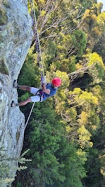 man in blue jacket and red helmet climbing on gray rocky mountain during daytime