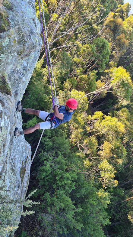 man in blue jacket and red helmet climbing on gray rocky mountain during daytime