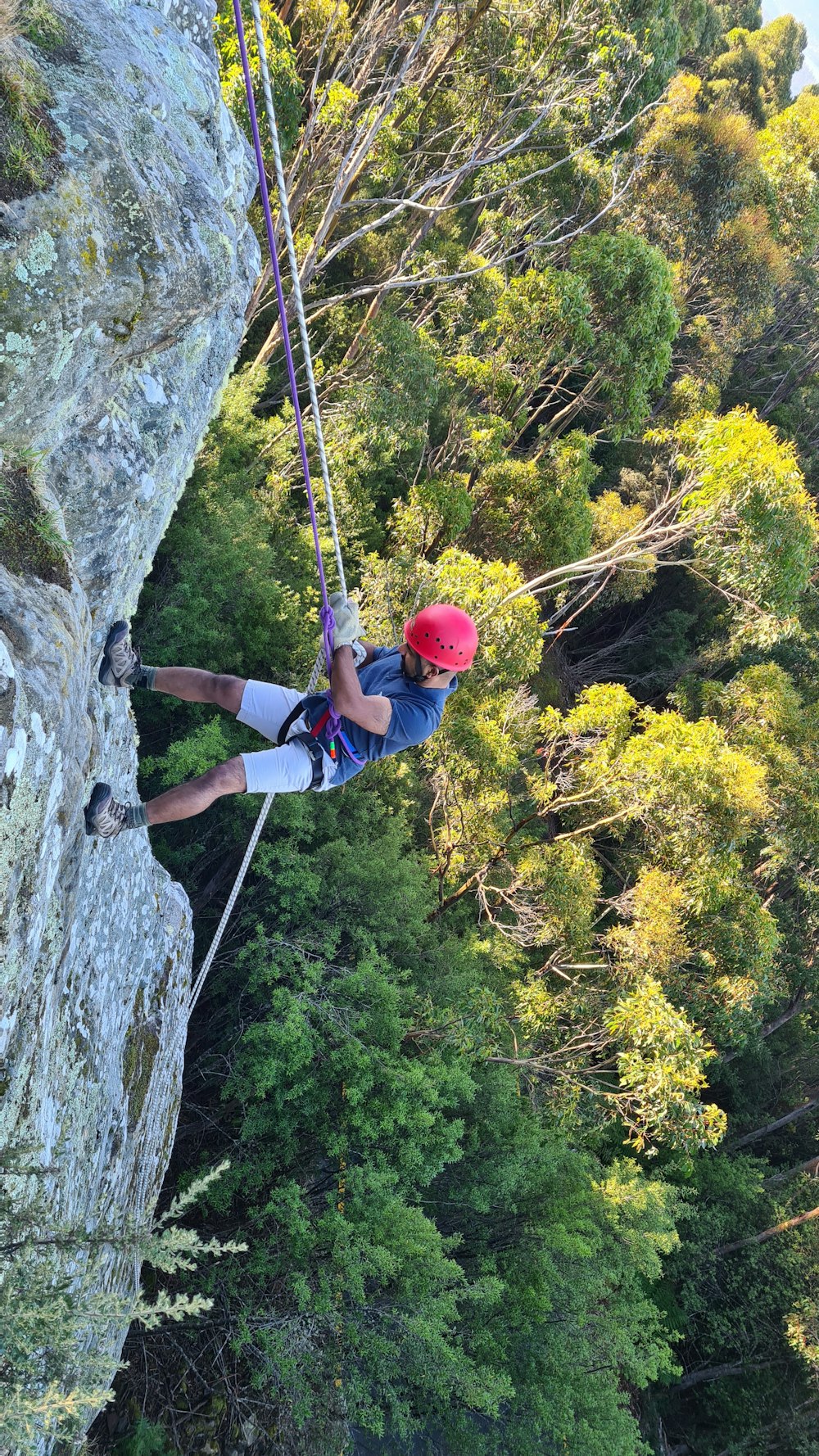 man in blue jacket and red helmet climbing on gray rocky mountain during daytime