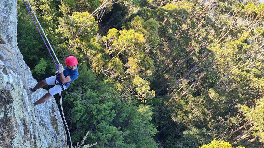 uomo in casco rosso e giacca nera che si arrampica sulla montagna