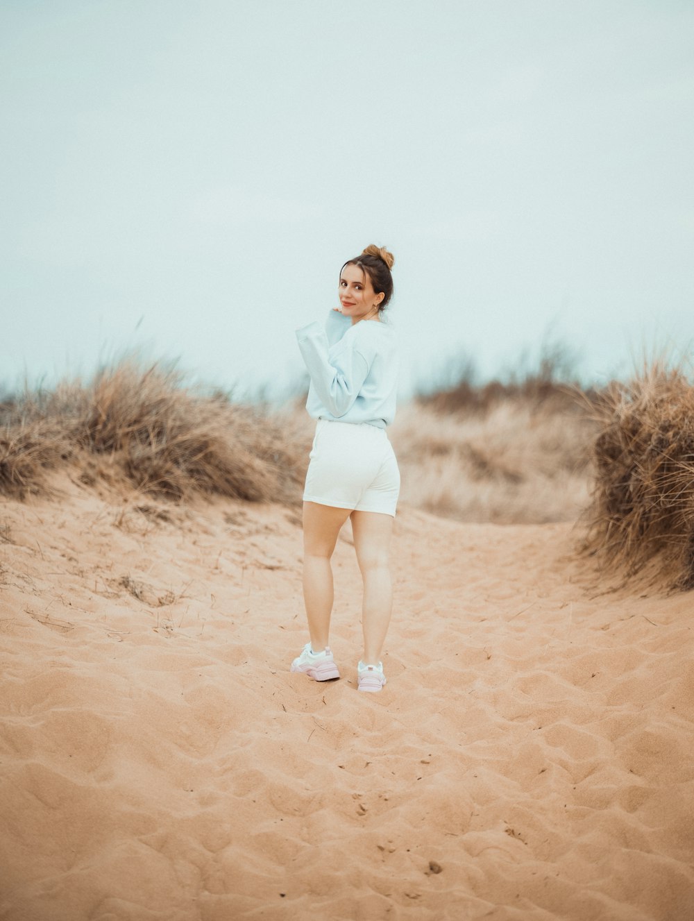 donna in camicia bianca a maniche lunghe e pantaloncini bianchi in piedi su sabbia marrone durante il giorno