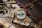 A collection of vintage nautical instruments arranged on a textured surface, including a brass compass, sextant, and an old telescope. These items rest on a burlap cloth alongside a leather-bound journal with a decorative ship wheel charm.