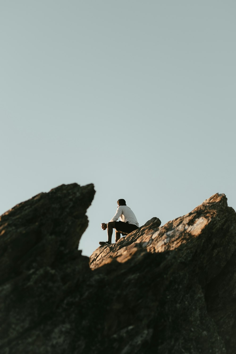Hombre en chaqueta negra sentado en la roca durante el día