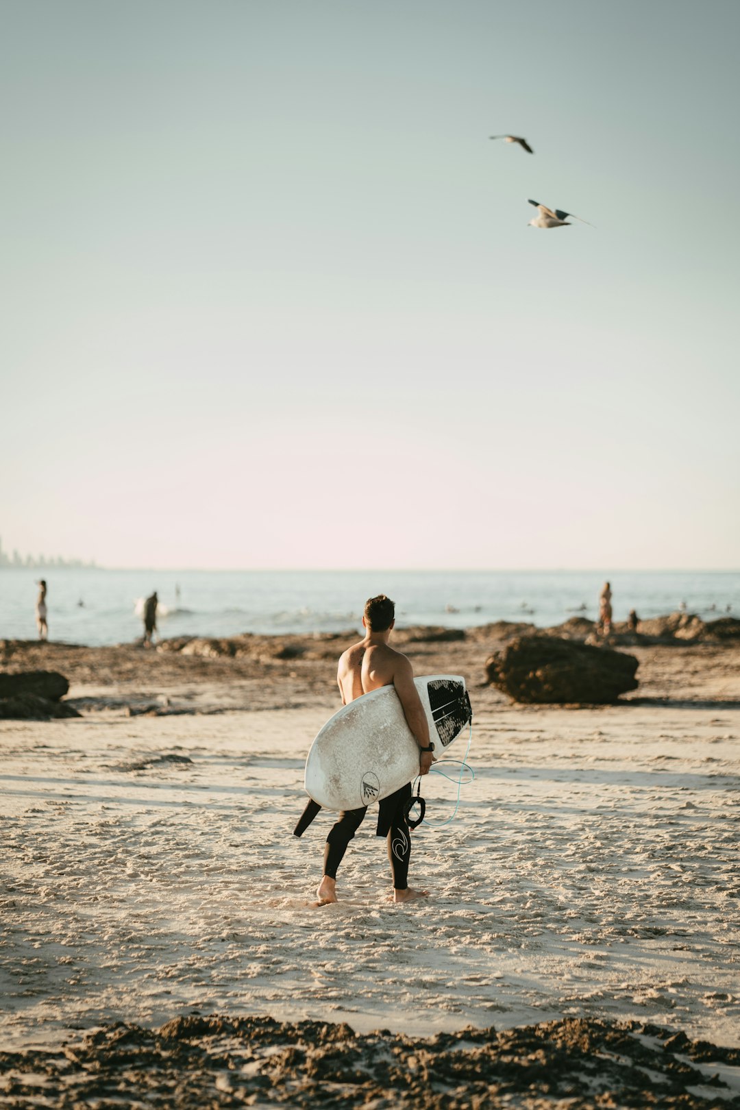 woman in white dress carrying white surfboard walking on beach during daytime