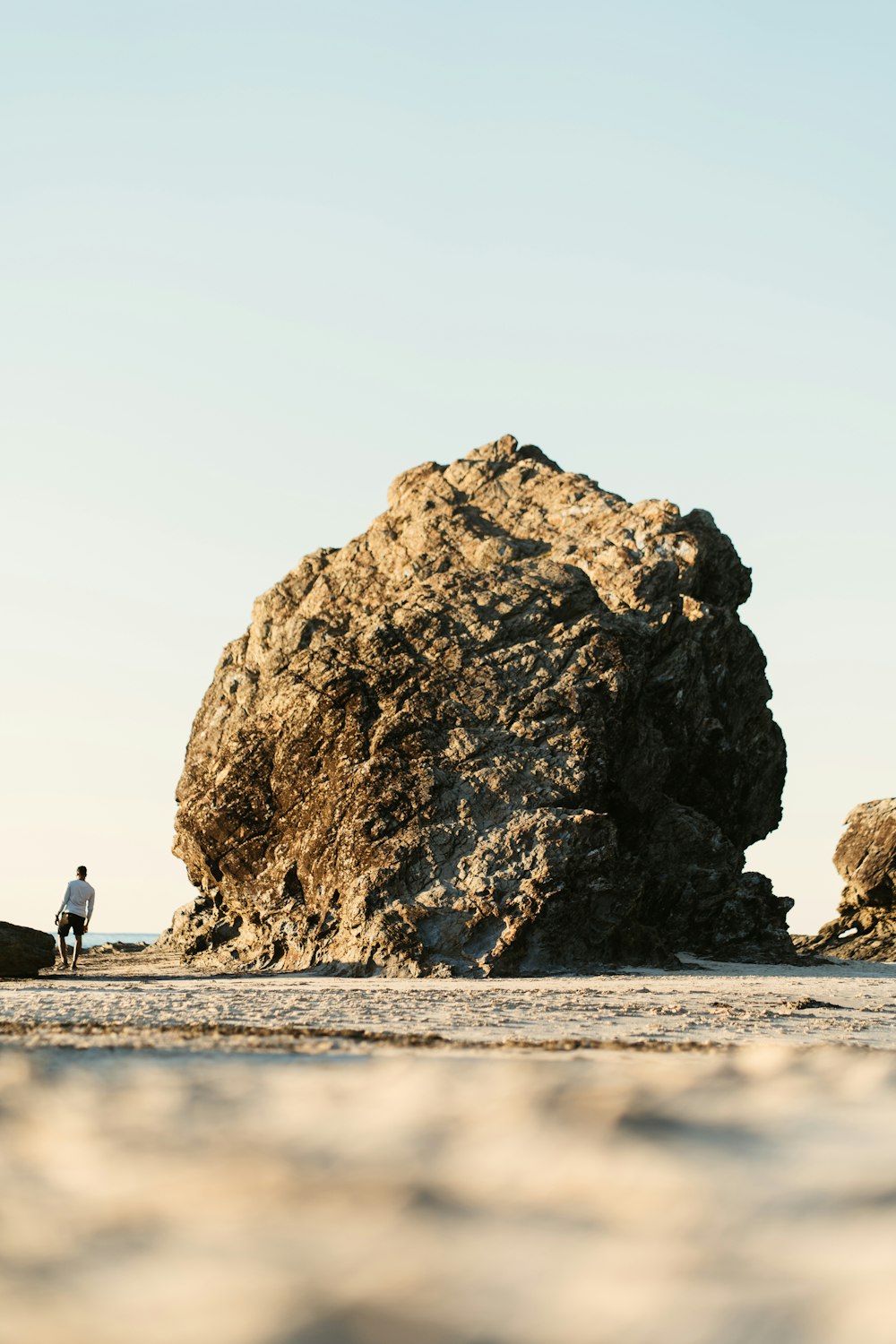 Personne en veste noire marchant sur la plage près de la formation de roche brune pendant la journée