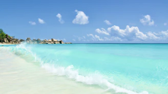 A quiet, pristine beach with turquoise waves gently lapping against untouched white sand under a clear blue sky.