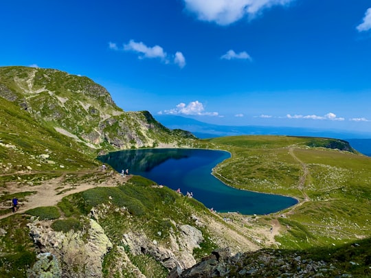 green and gray mountain beside blue lake under blue sky during daytime in Rila National Park Bulgaria