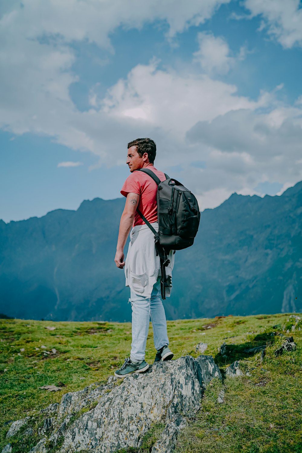 man in red t-shirt and white pants with black backpack standing on green grass field