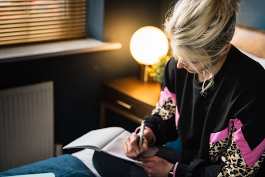 A thoughtful young woman journaling her fitness progress in a cozy, sunlit room.