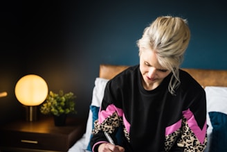 A serene boho chic woman journaling in a softly lit taupe and pink room.