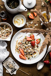 A sunlit breakfast table set with fresh Greek yogurt, honey, seasonal fruits, and a cup of coffee, overlooking the old town of Nafplio.