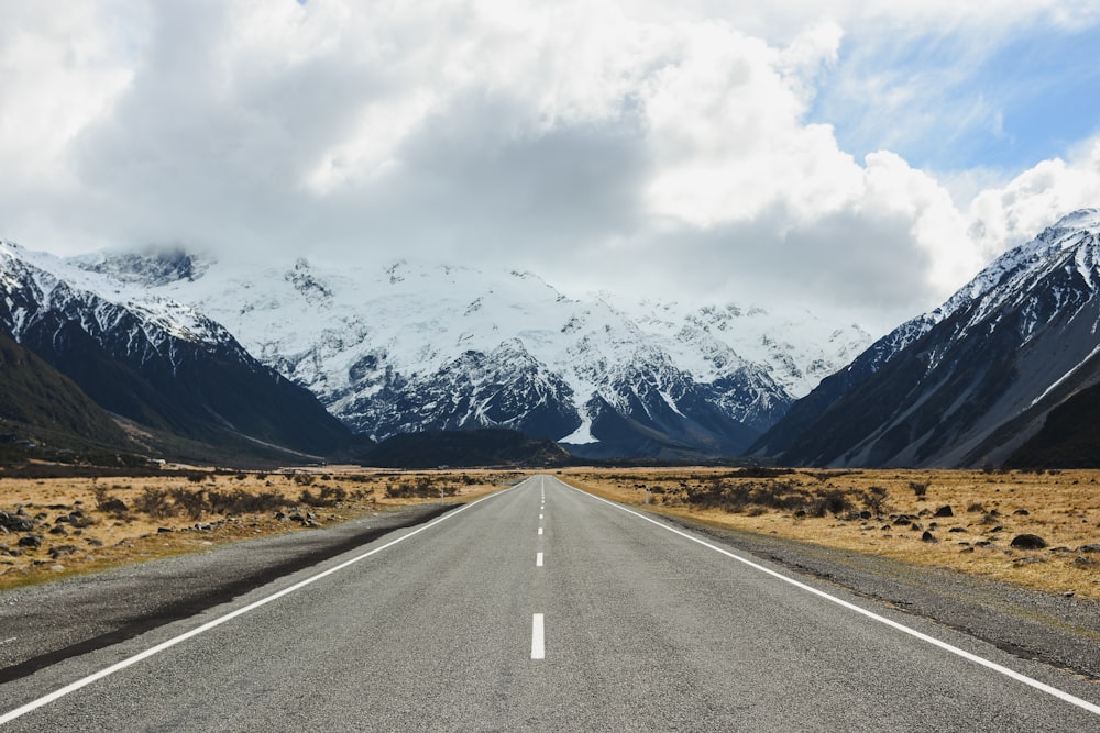 gray concrete road near mountain under white clouds during daytime