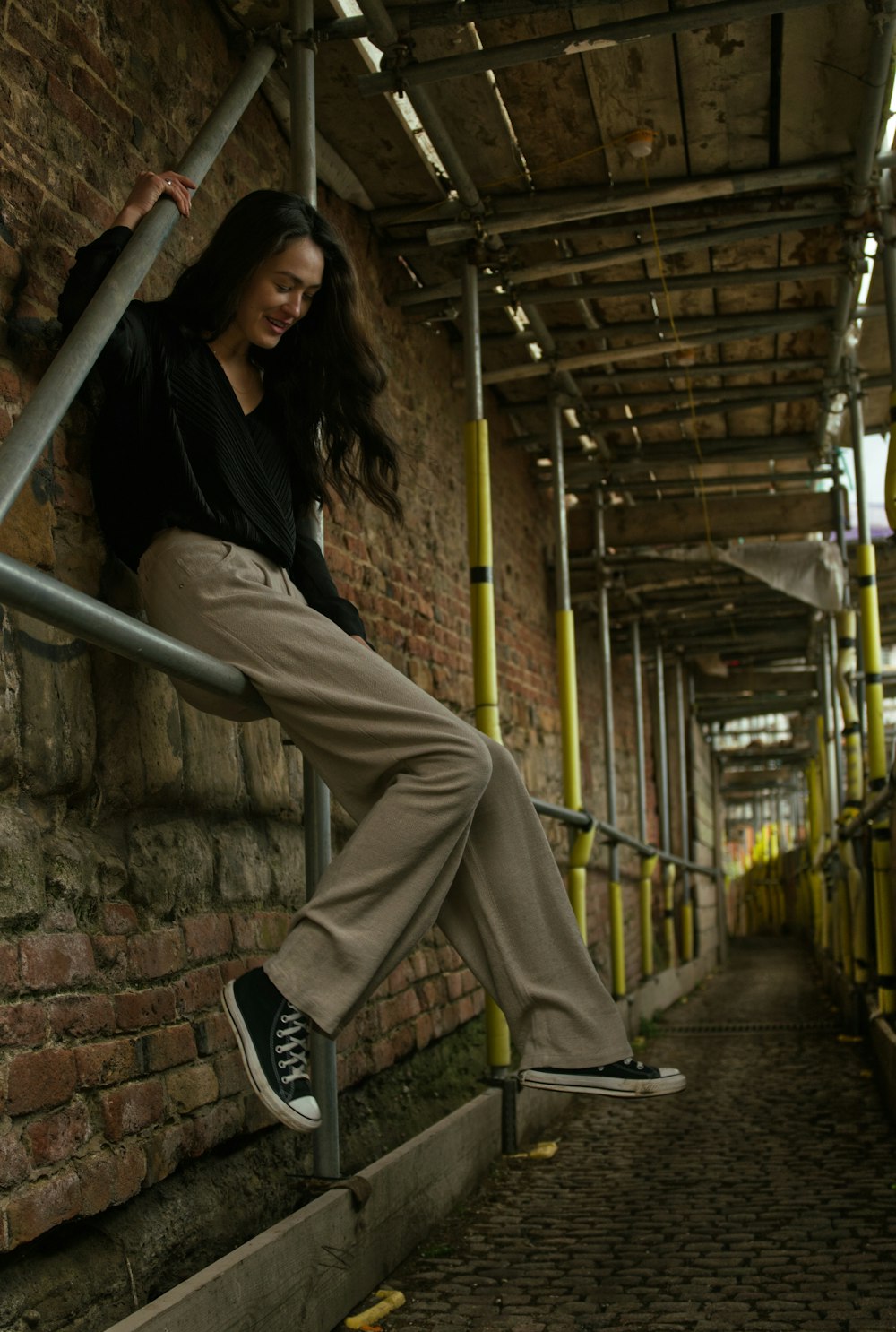 woman in black shirt and beige pants sitting on metal bar