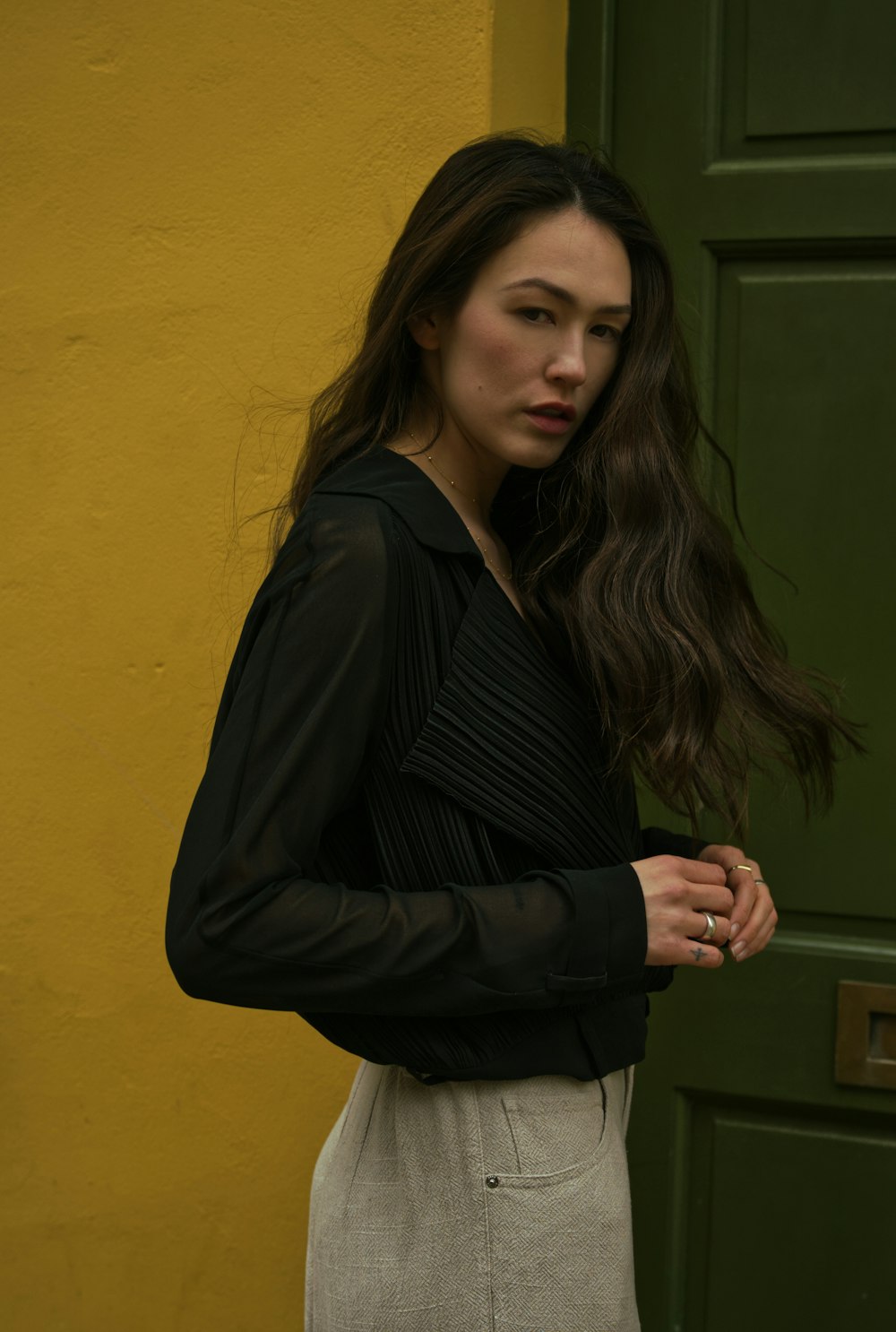 woman in black blazer standing near yellow wall