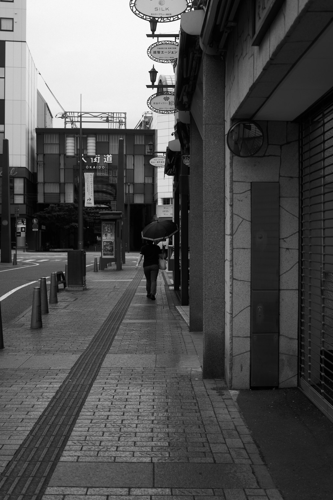 grayscale photo of person walking on sidewalk