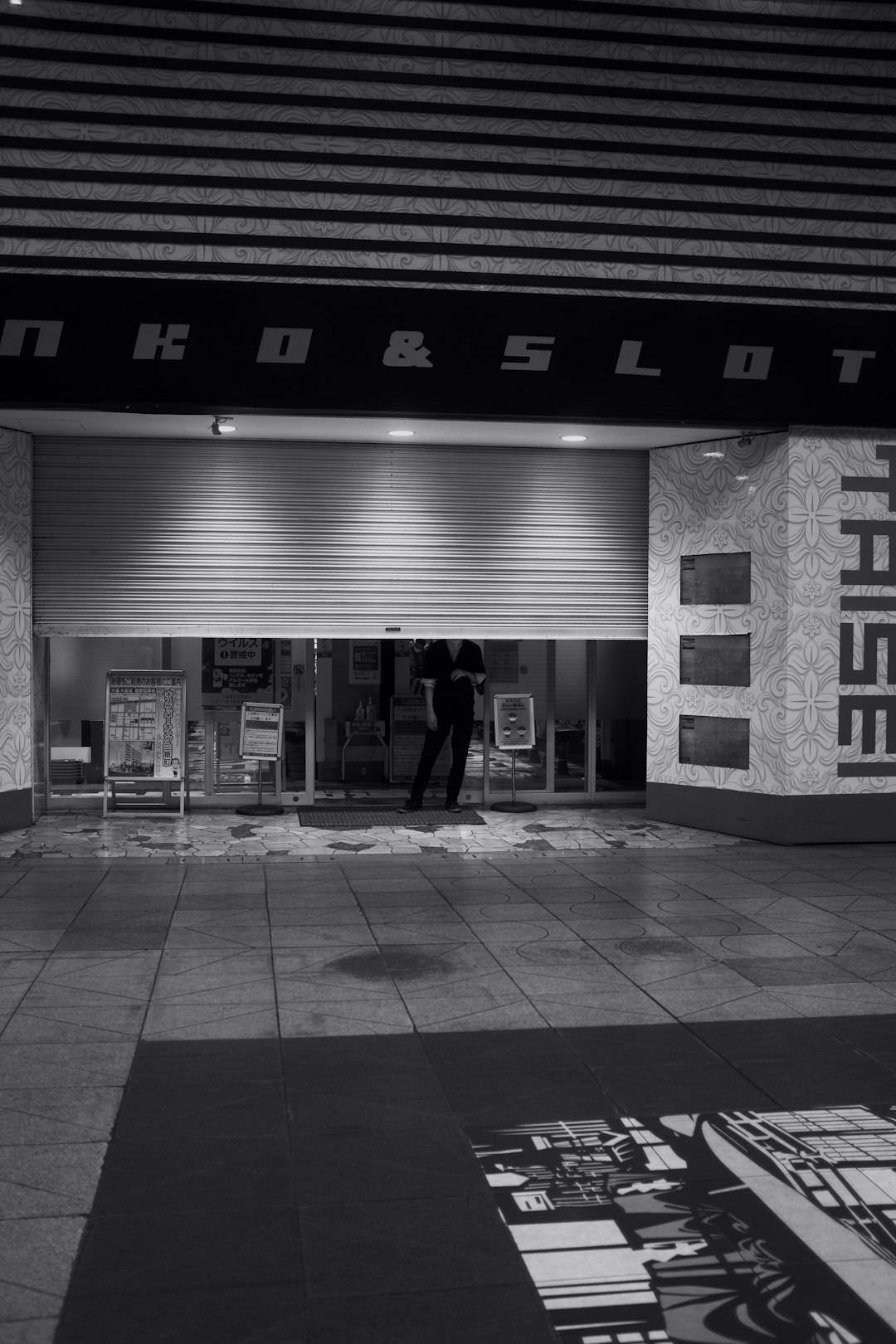 grayscale photo of man in black jacket standing in front of store