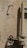A weathered metal valve attached to an old pipe, mounted on a rough, beige-colored concrete wall. The shadows of the valve and pipe create stark contrasts on the wall.
