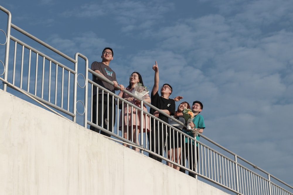 3 men and 2 women standing on white concrete wall during daytime