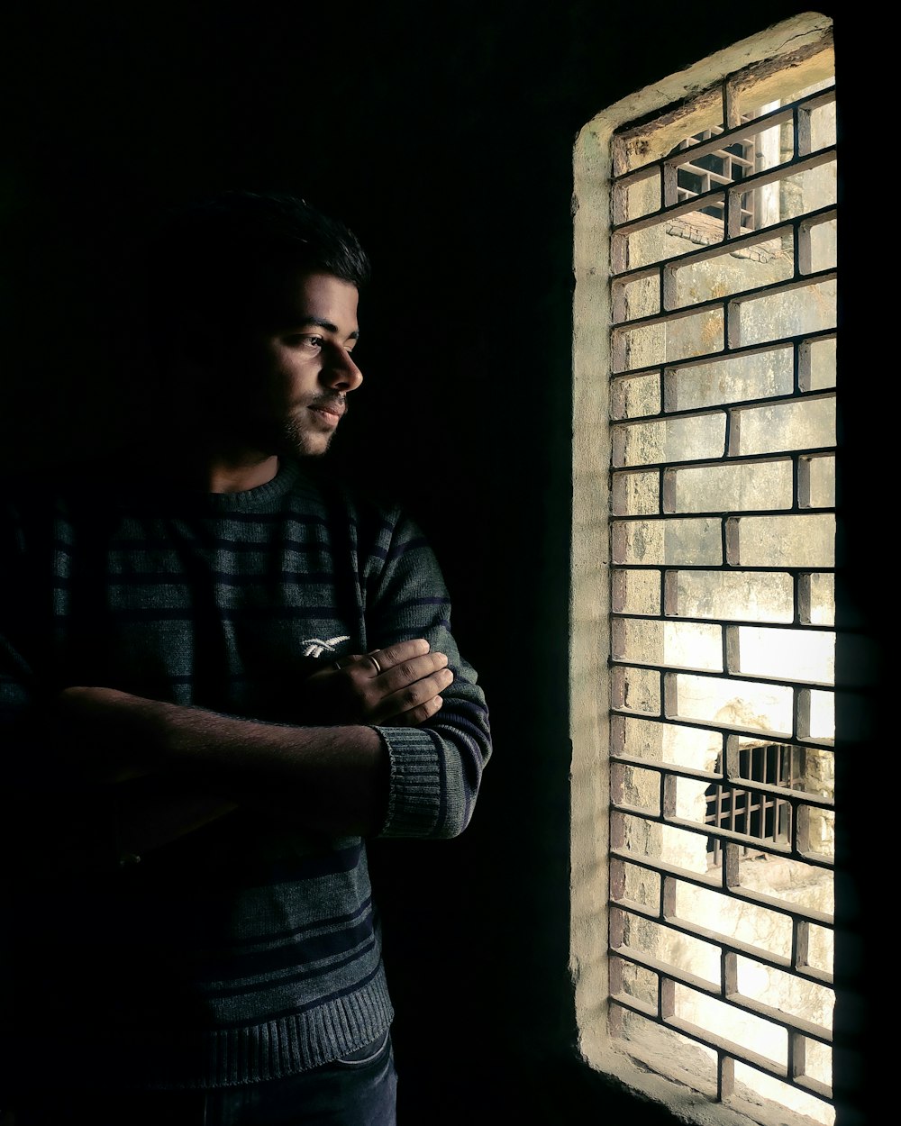 man in gray long sleeve shirt standing beside brown brick wall