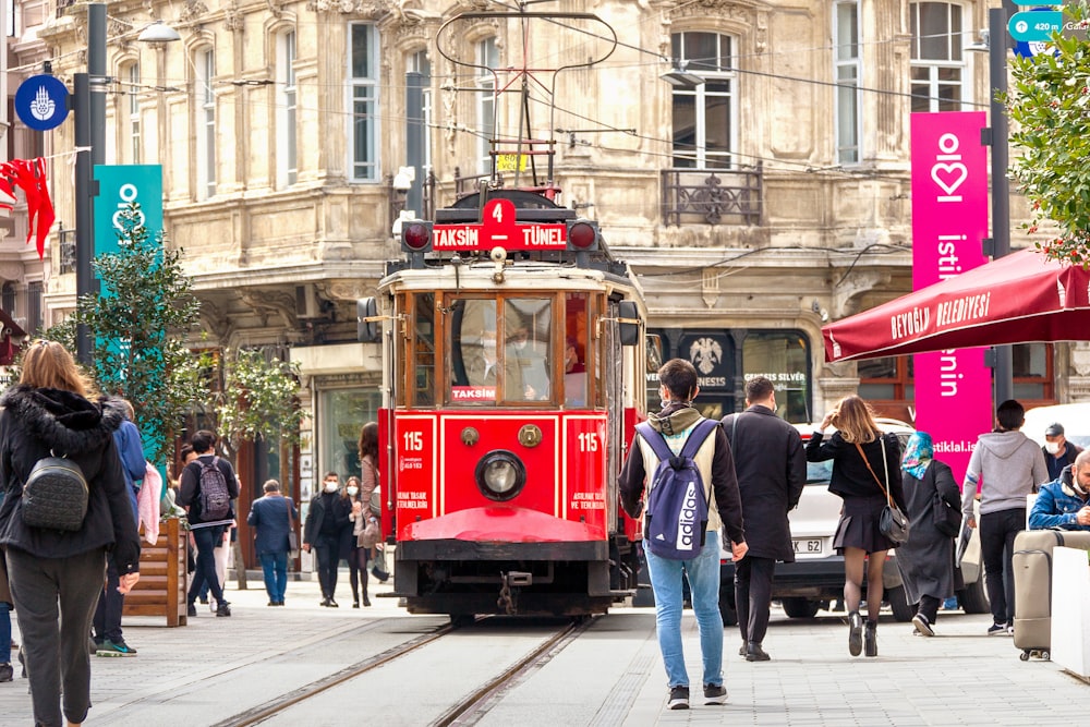 people walking on sidewalk near red tram during daytime