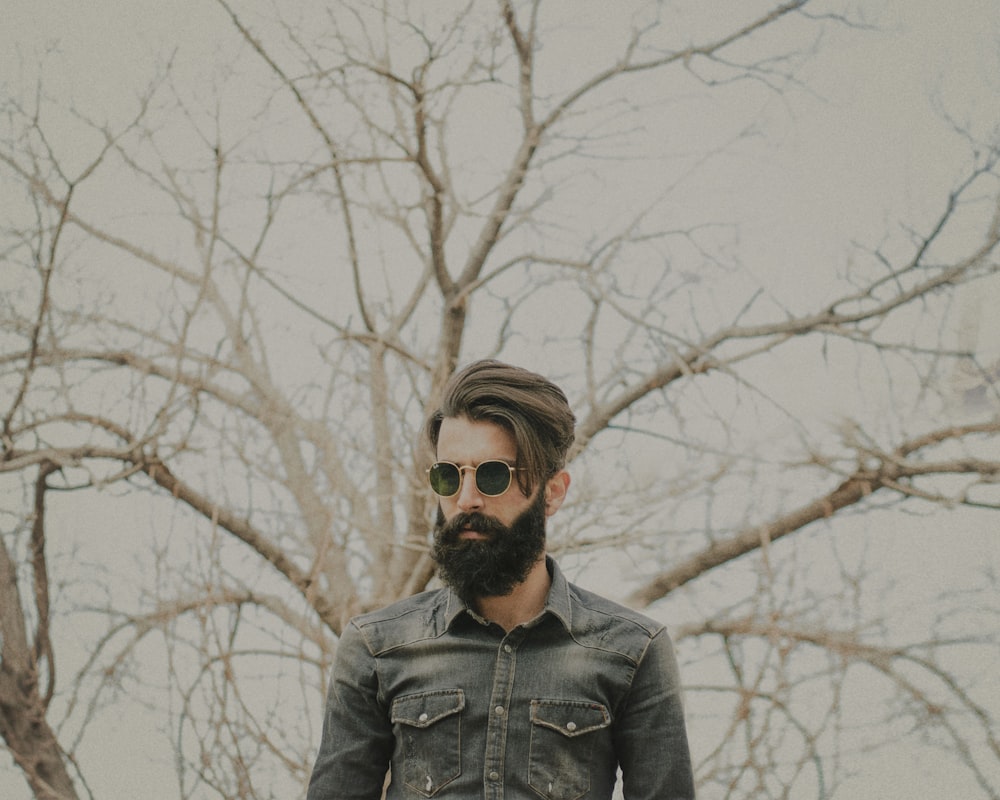 man in black leather jacket wearing black sunglasses standing near bare trees during daytime