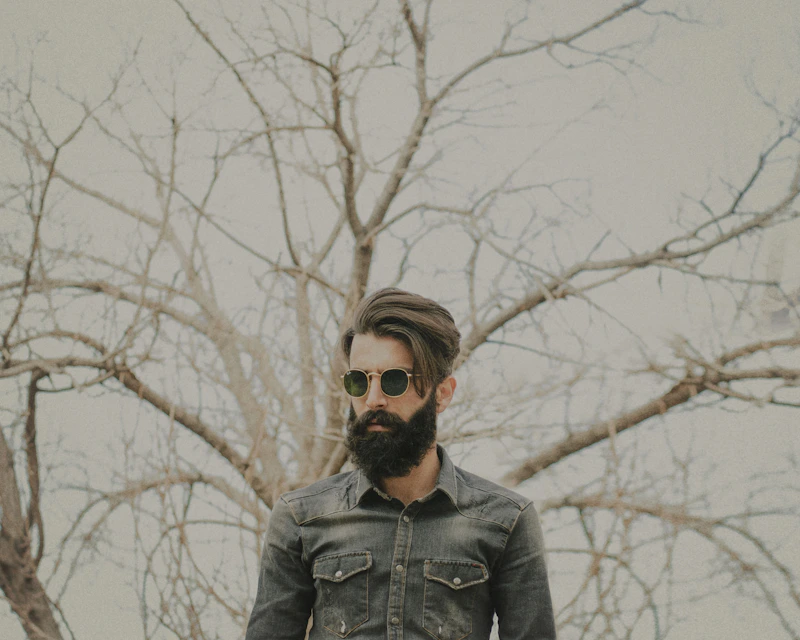 man in a black leather jacket and sunglasses near bare trees