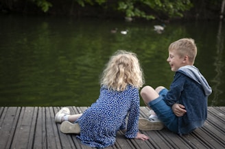 girl in blue and white floral dress sitting on brown wooden dock during daytime