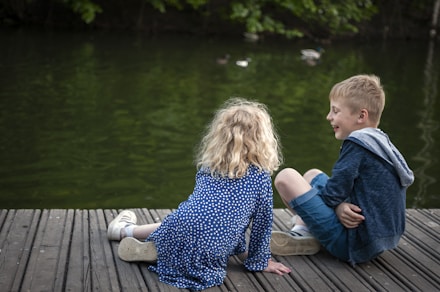 girl in blue and white floral dress sitting on brown wooden dock during daytime