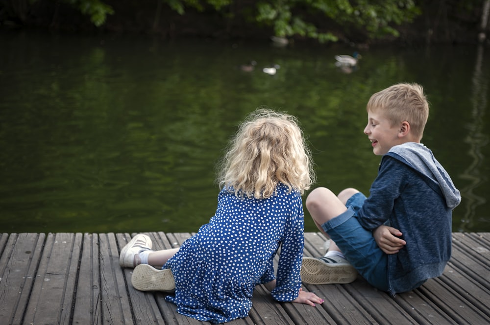 fille en robe à fleurs bleu et blanc assise sur le quai en bois brun pendant la journée