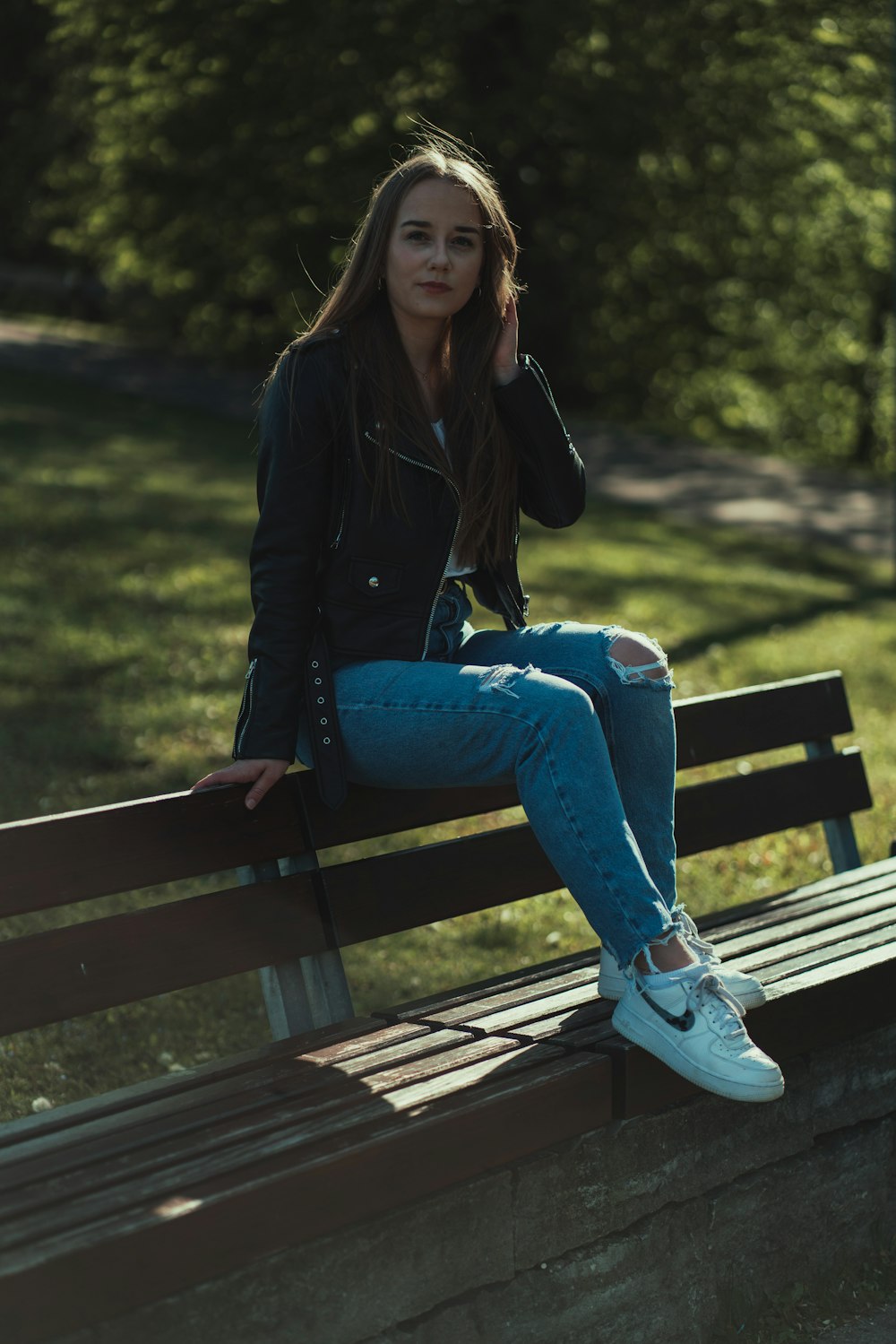 Frau in schwarzer Jacke und blauer Jeans sitzt auf brauner Holzbank