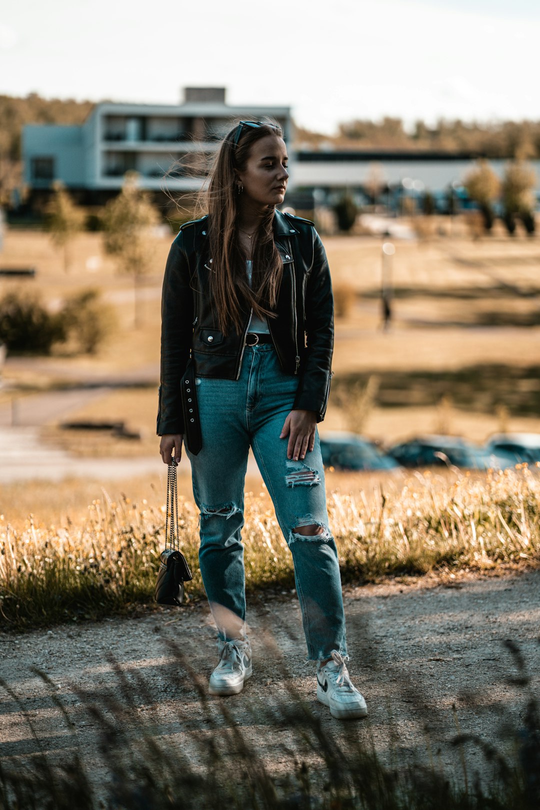 woman in black leather jacket and blue denim jeans walking on dirt road during daytime