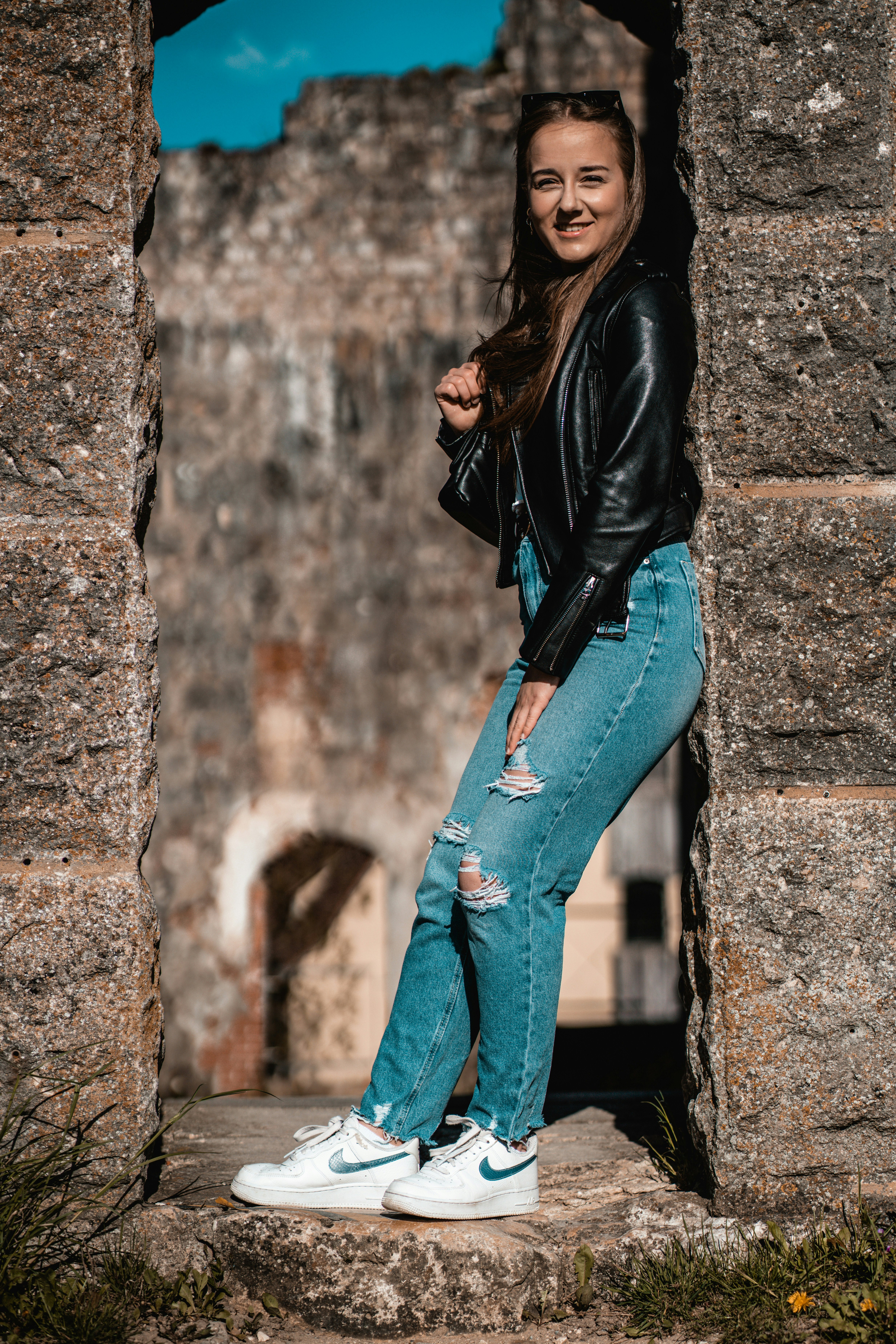 woman in black leather jacket and blue denim jeans leaning on wall