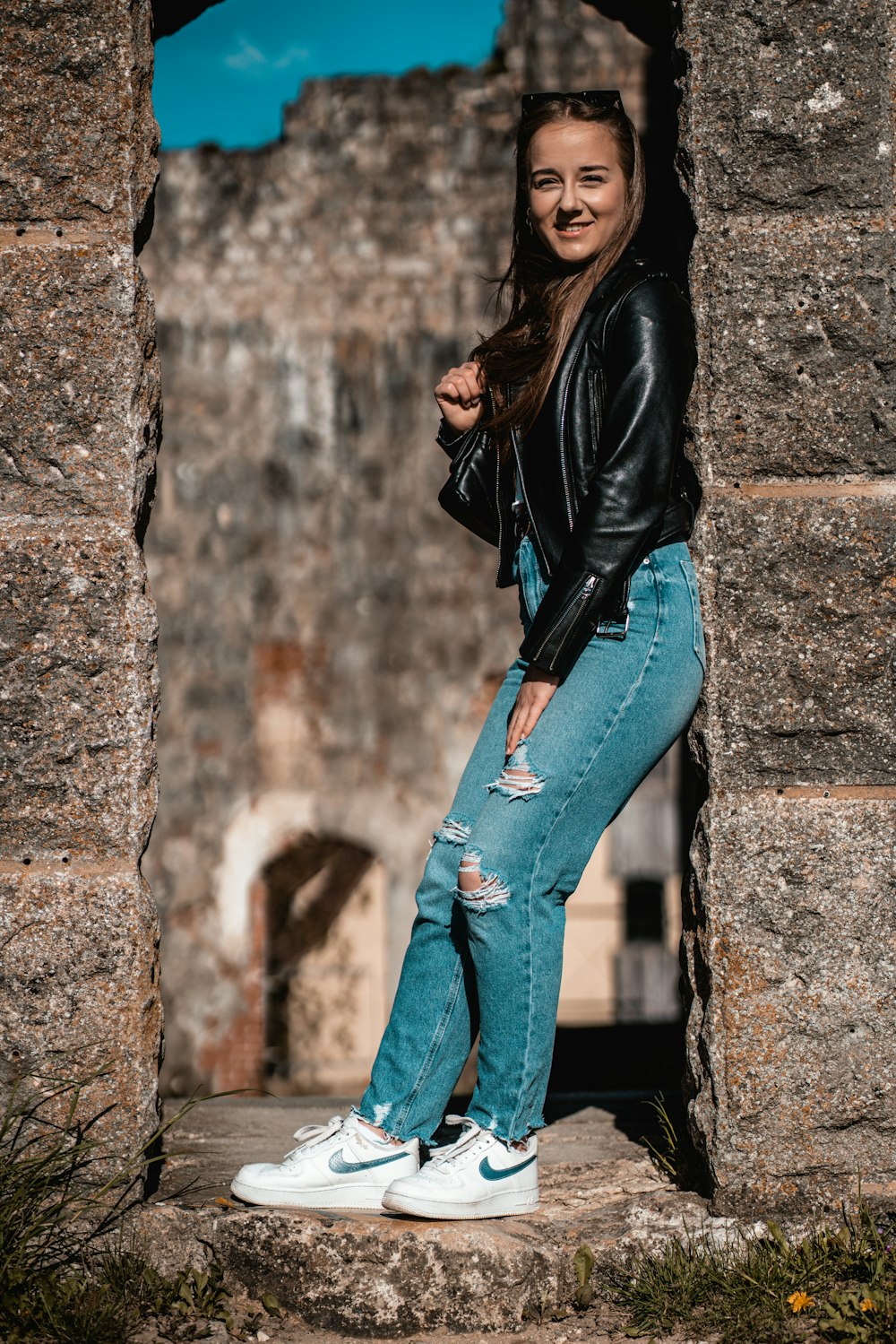 woman in black leather jacket and blue denim jeans leaning on wall